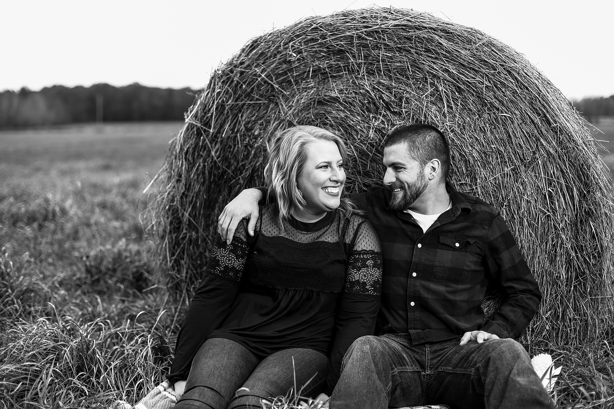 engaged couple smiling while sitting in front of a hay bale