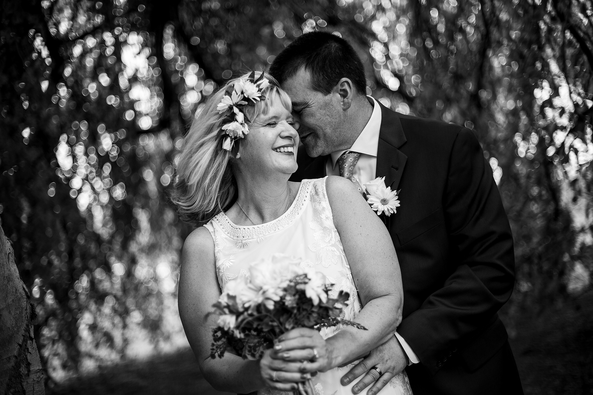 Couple standing under willow tree and smiling at their wedding at the Schoolhouse