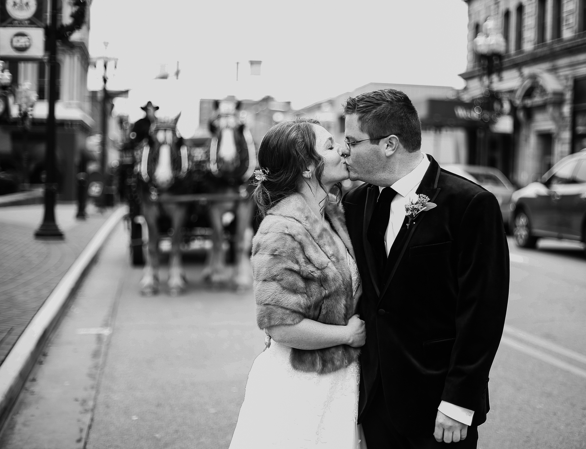 Bride and groom kiss with horse drawn carriage in the background