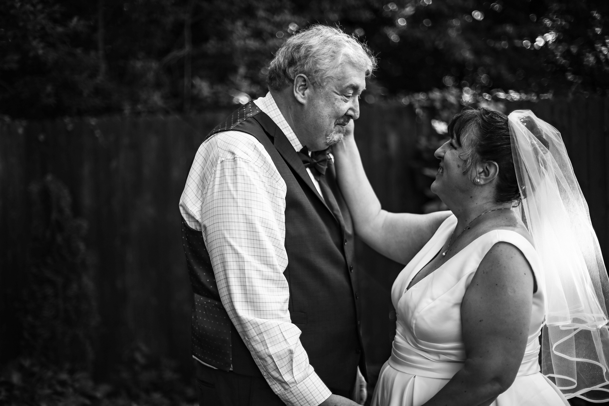 Bride touches groom's cheek during first look portraits before their intimate back garden wedding