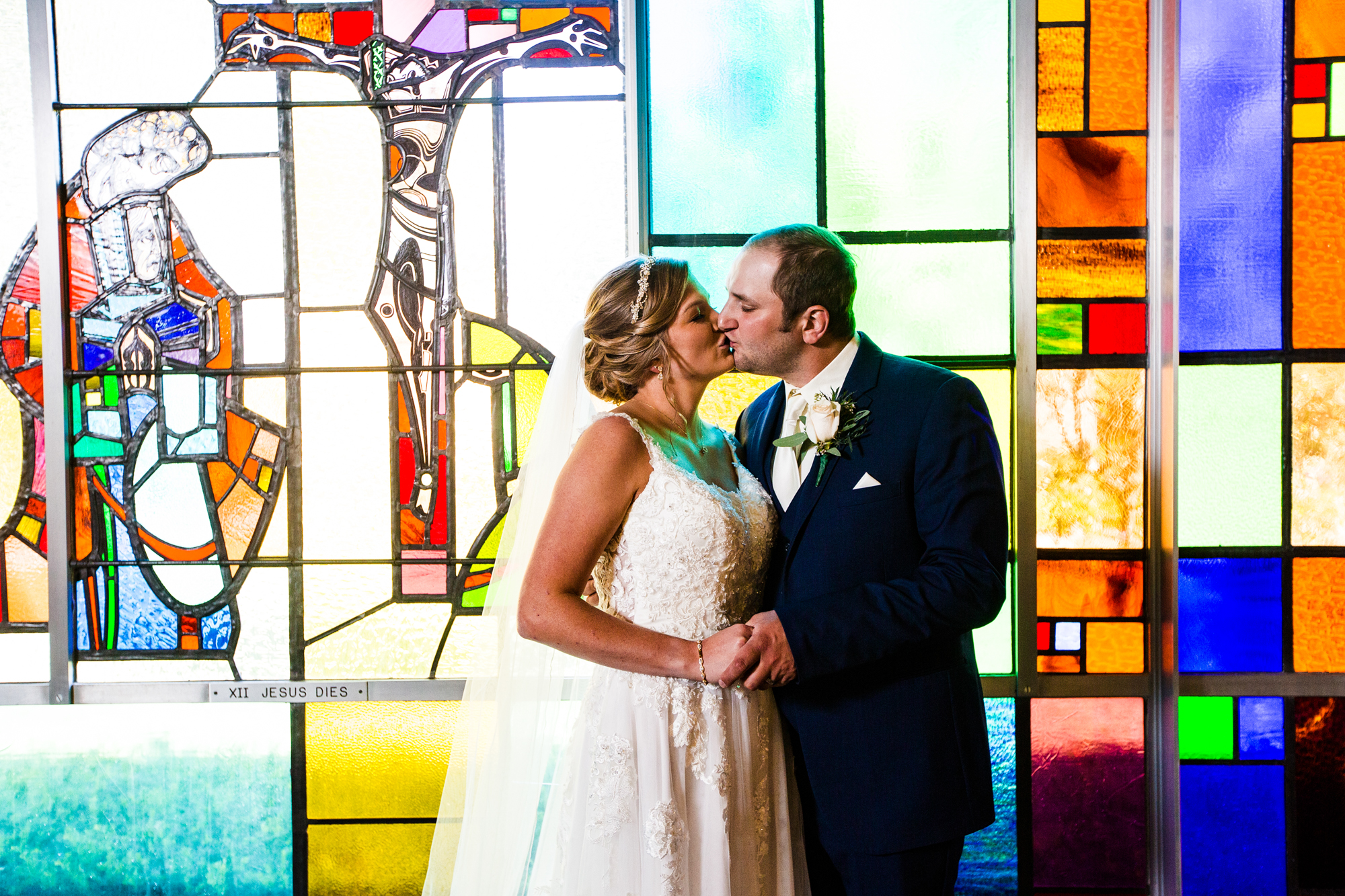 Bride and groom kiss next to stained glass at their St George Church wedding