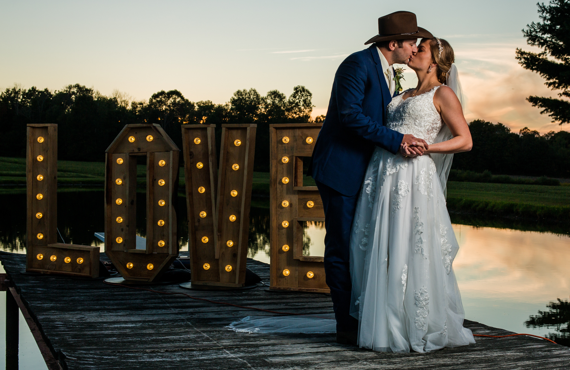 Bride and groom kissing next to giant lighted LOVE sign at sunset during their wedding reception on family farm in Waterford, PA