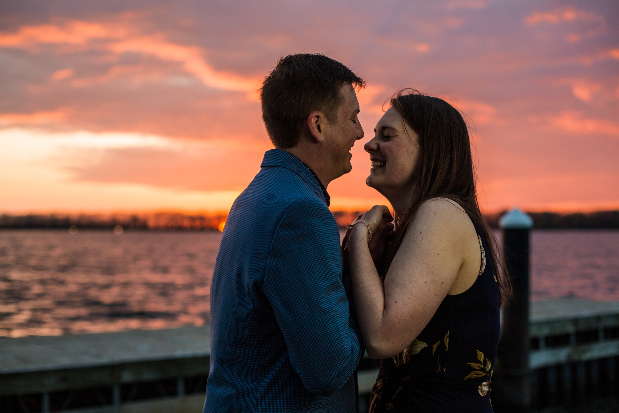 Couple laugh and hold hands at sunset for engagement photos at Erie Yacht Club