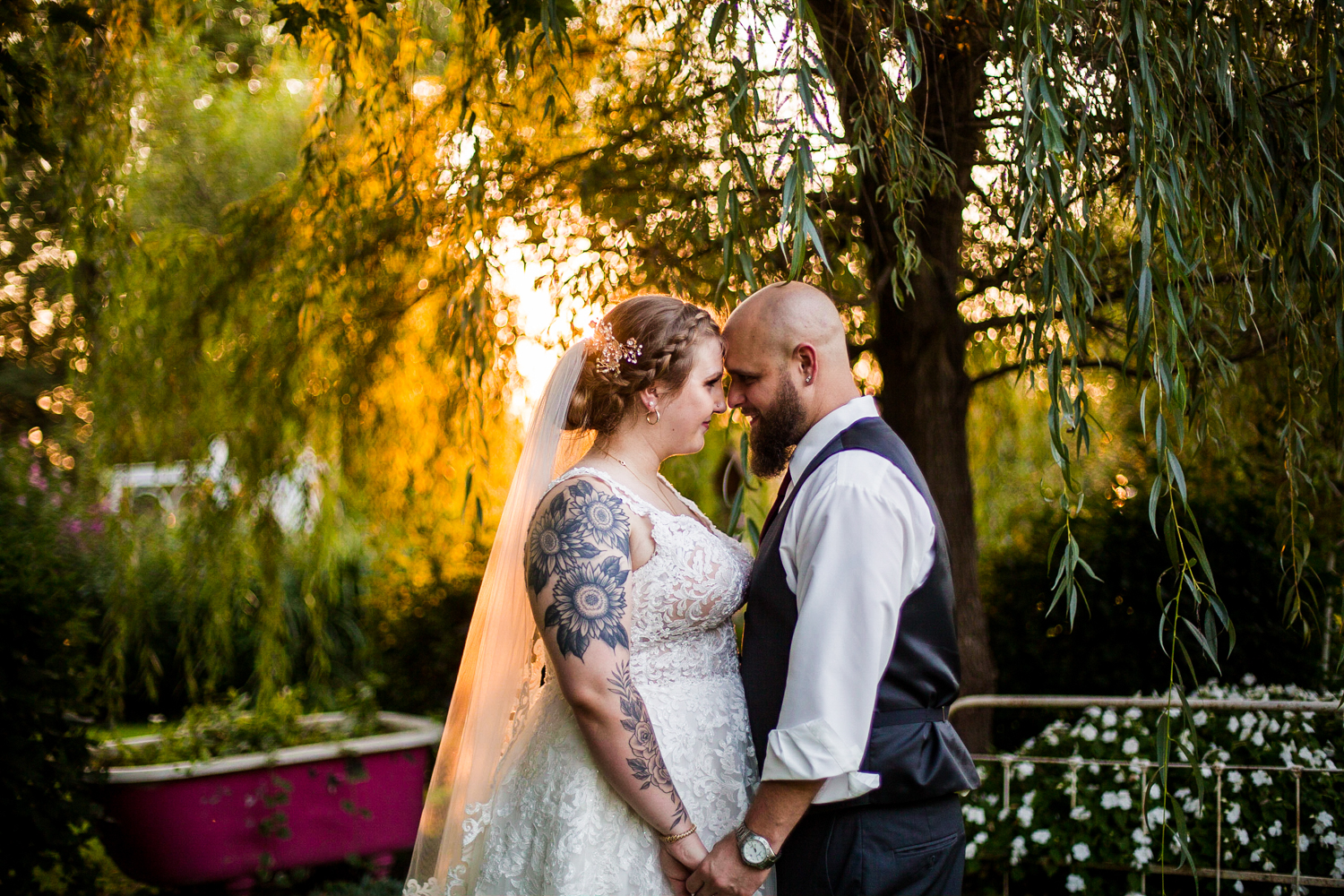 Bride and groom touching foreheads while sun peeks through the trees during wedding at Whispering Trees Manor