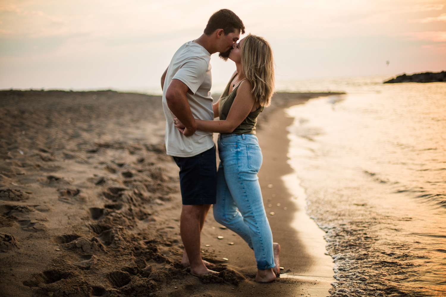 Couple kissing next to Lake Erie as the sun sets for Lighthouse Beach engagement photos