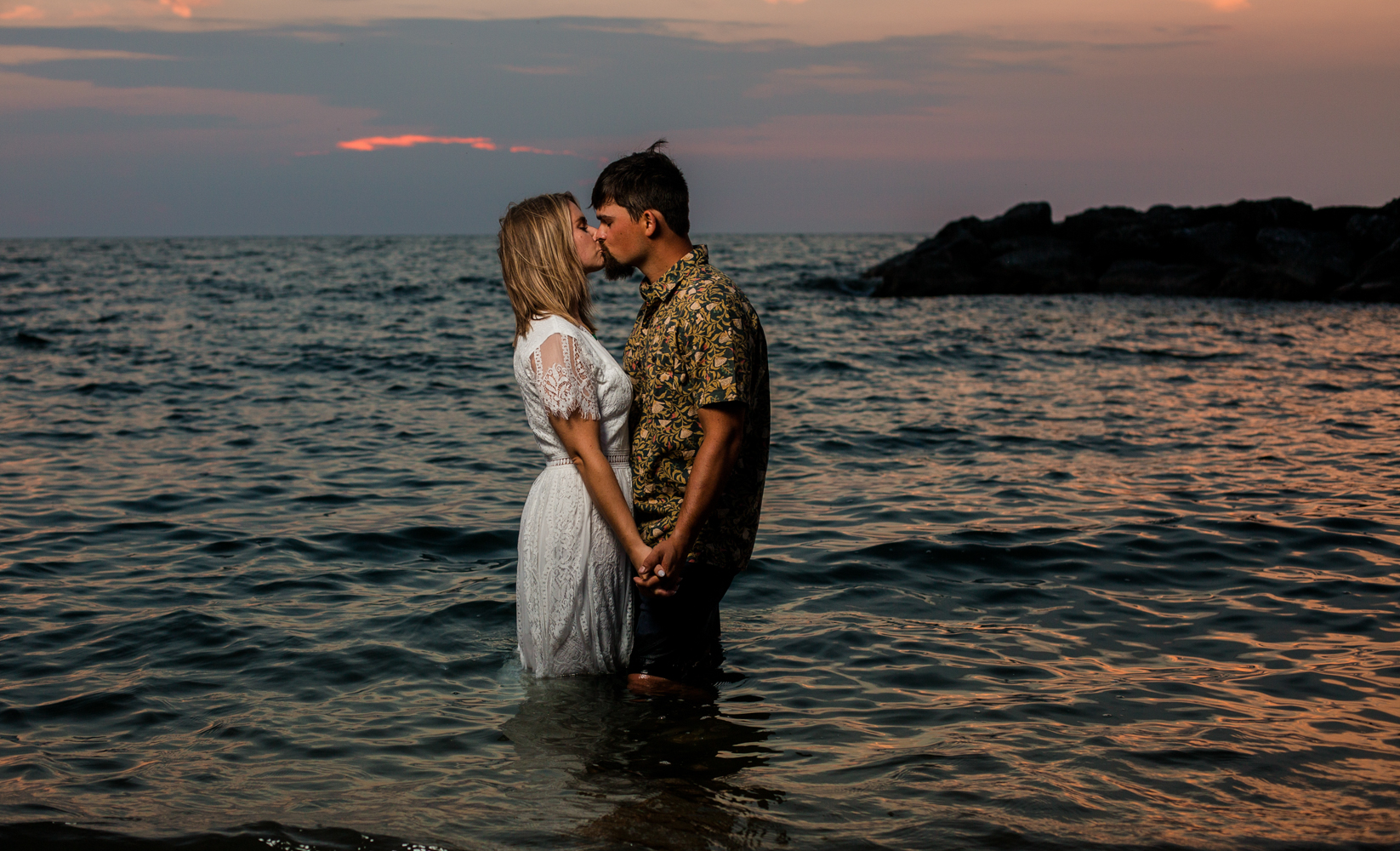 Man and woman kissing while standing in Lake Erie at sunset for Lighthouse Beach engagement photos