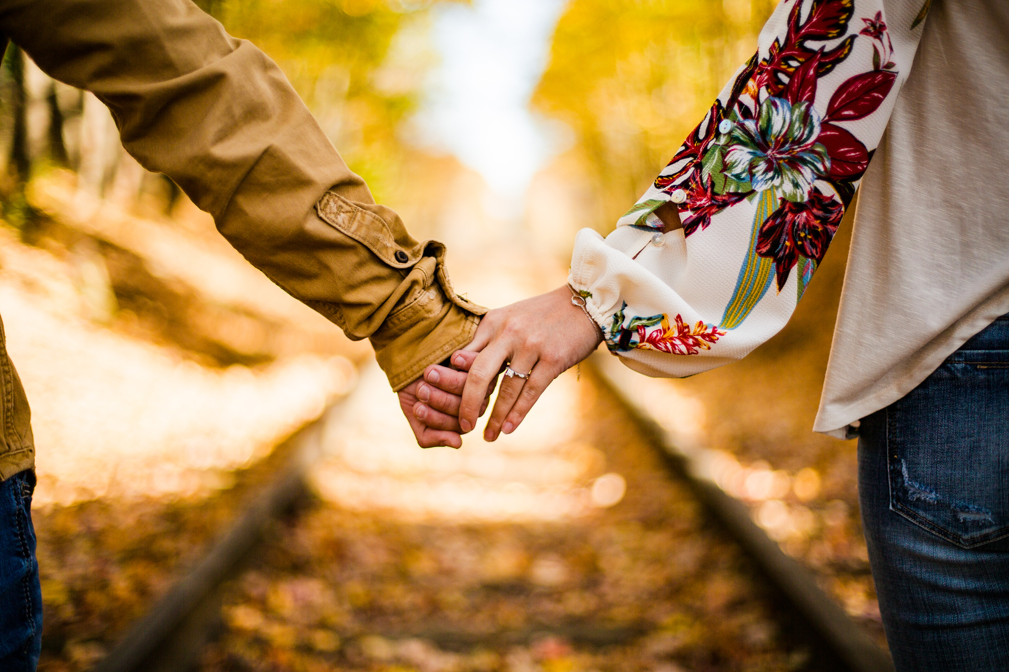 Hands clasped in front of abandoned railroad tracks during a couple's engagement photo session