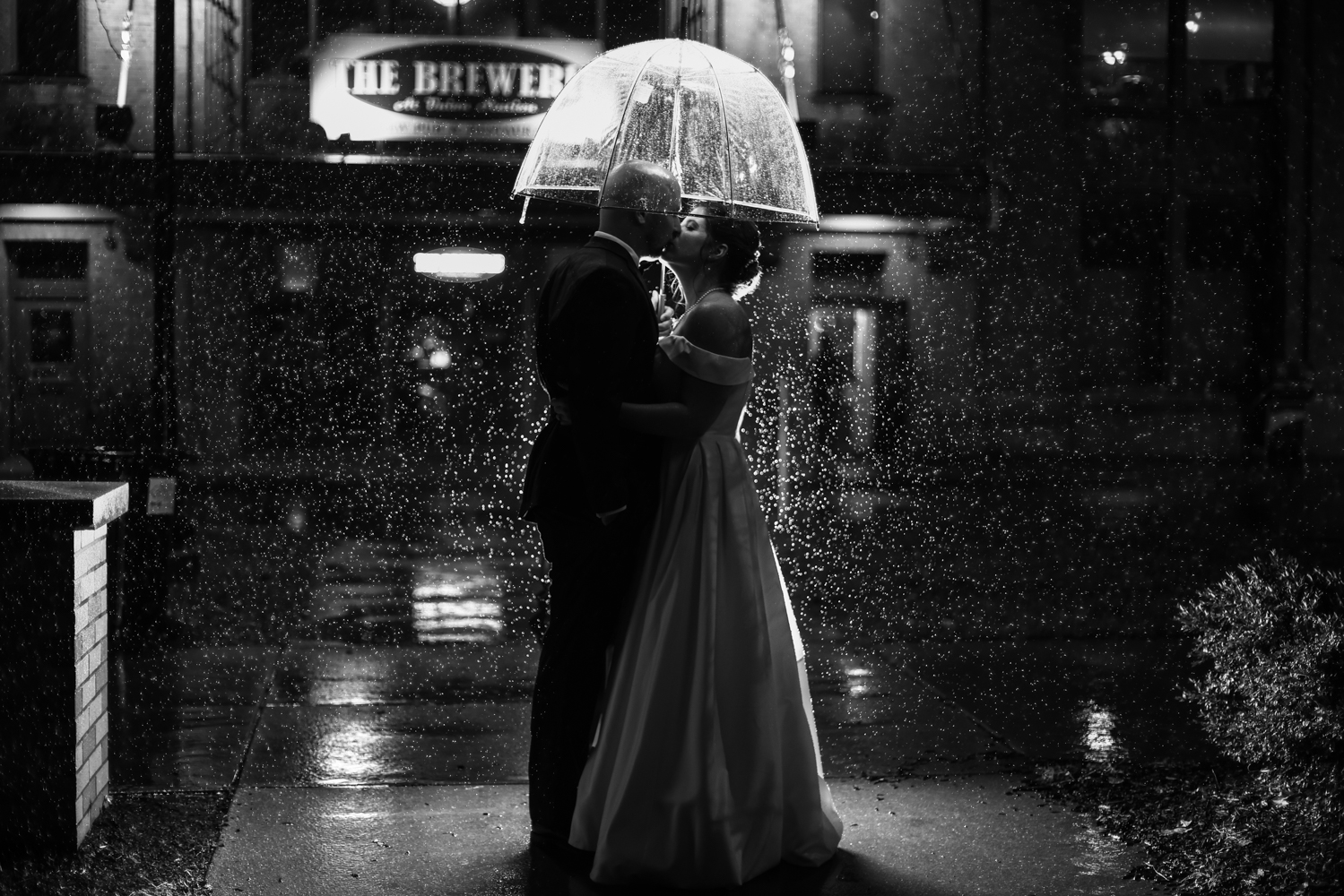 Bride and groom kiss under an umbrella at night outside the Brewerie at Union Station