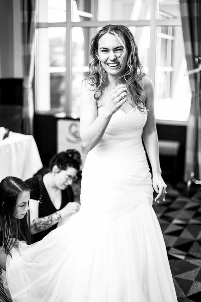 Photography assistants help to bustle bride's dress as she laughs at the camera